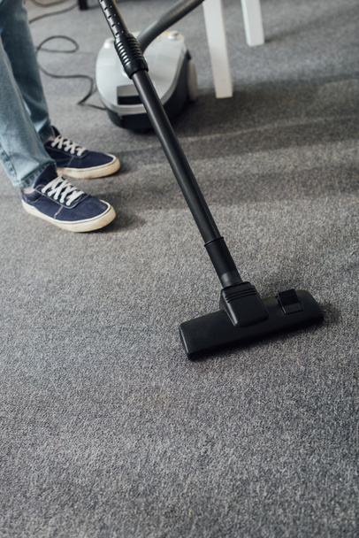 Vue recadrée de l'homme nettoyage tapis dans le salon avec aspirateur
  - Photo, image