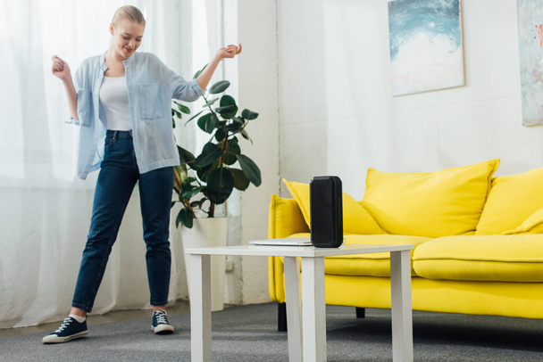 Attraktive Frau tanzt neben tragbarem Lautsprecher und Laptop auf Couchtisch im Wohnzimmer - Foto, Bild
