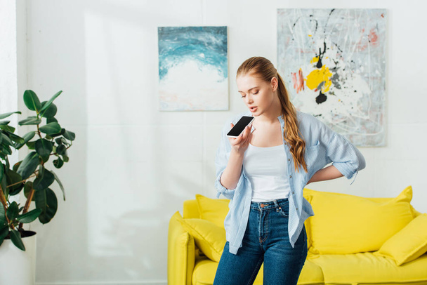 Beautiful woman using speakerphone while having conversation on smartphone in living room - Valokuva, kuva