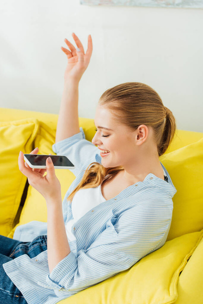 Side view of happy girl holding smartphone on couch  - Foto, Imagem