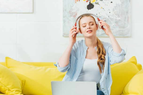 Beautiful woman listening music in headphones near laptop at home - Photo, Image