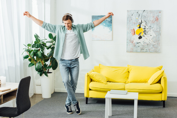 Handsome man dancing while listening music in headphones in living room - Fotoğraf, Görsel