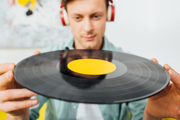 Selective focus of young man in headphones holding vinyl record at home - Fotografie, Obrázek