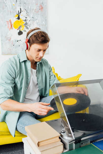 Homme dans les écouteurs en utilisant un tourne-disque près des livres sur la table basse dans le salon
 - Photo, image