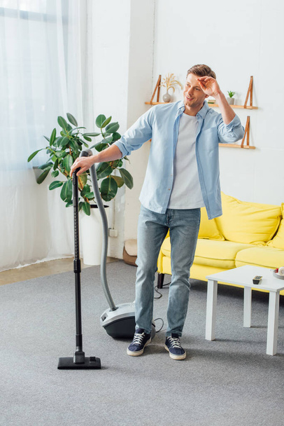 Man smiling away while using vacuum cleaner in living room - Fotoğraf, Görsel