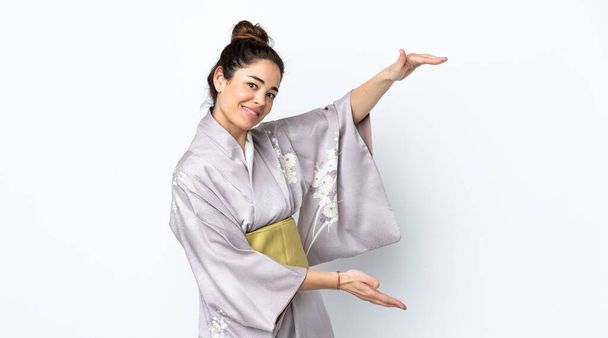 Woman wearing kimono over isolated background holding copyspace to insert an ad - Foto, afbeelding