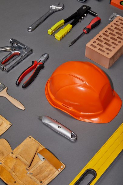 tendido plano con casco naranja, cinturón de herramientas, ladrillo, herramientas industriales y cepillo sobre fondo gris
 - Foto, imagen