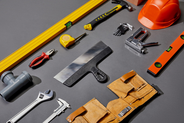 płaska leżanka z kaskiem, paskiem narzędziowym i narzędziami przemysłowymi na szarym tle  - Zdjęcie, obraz
