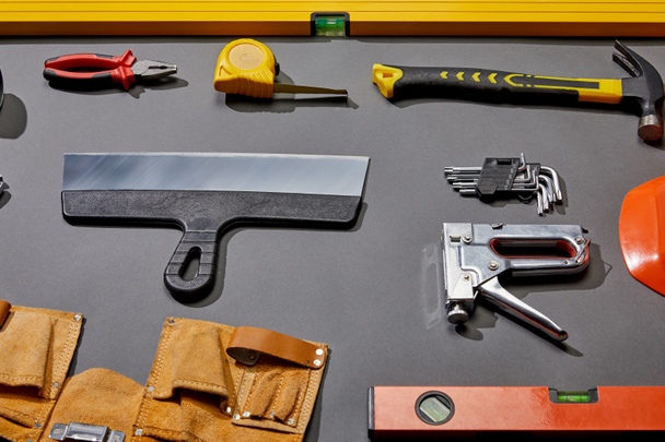 high angle view of spirit levels, pliers, measuring tape, hammer, putty knife, angle keys, stapler and tool belt on grey background  - Photo, Image