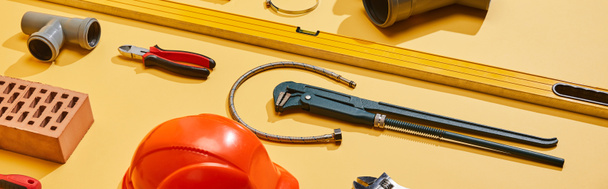 Panoramaaufnahme von Wasserwaage, Bremssätteln, Sanitärschlauch, Rohrverbinder, Ziegel, Zange und Affenschlüssel auf gelbem Hintergrund - Foto, Bild