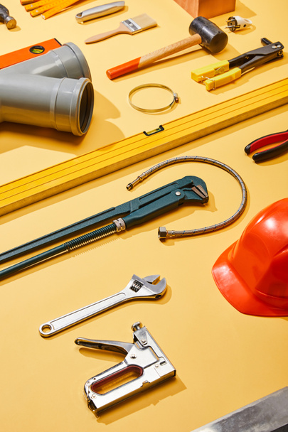 visão de alto ângulo de ferramentas industriais, mangueira de encanamento, capacete e escova no fundo amarelo
 - Foto, Imagem