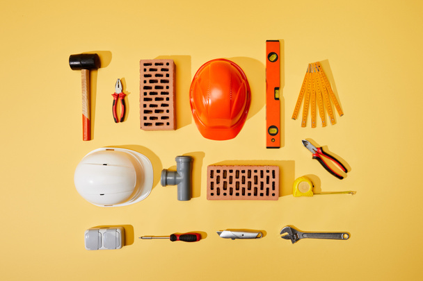 Ansicht von Ziegeln, Helmen, Maßband und Industriewerkzeugen auf gelbem Hintergrund - Foto, Bild