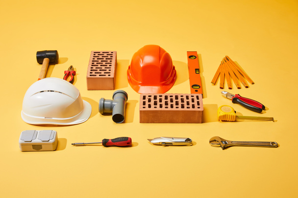 tendido plano con ladrillos, cascos, herramientas industriales y cinta métrica sobre fondo amarillo
 - Foto, Imagen
