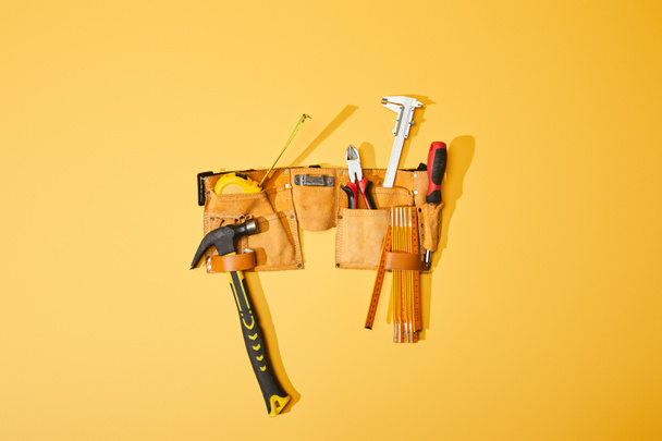 top view of tool belt with hammer, pliers, measuring tape, calipers, screwdriver and folding ruler on yellow background - Photo, Image