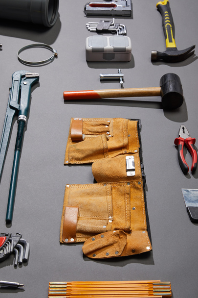 high angle view of tool belt, hammers, monkey wrench, putty knife, pliers, calipers, rivet gun, angle keys and stapler on grey background - Photo, Image