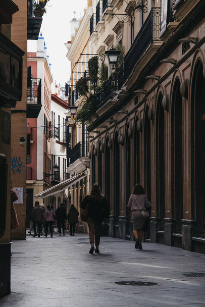 Seville, Spain - January 17, 2020: Rear view of women walking on a street in Seville, the capital of Andalusia region in Southern Spain and a popular tourist destination. Motion blur, selective focus. - Photo, Image
