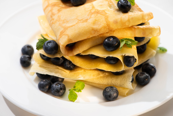 close up view of tasty crepes with mint and blueberries on plate on white background - Fotó, kép
