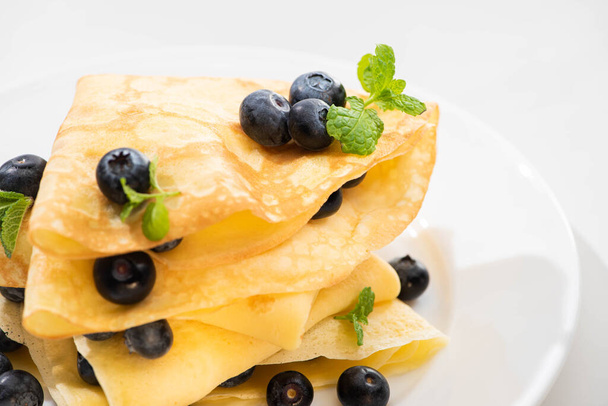 close up view of tasty crepes with mint and blueberries on plate on white background - Fotografie, Obrázek