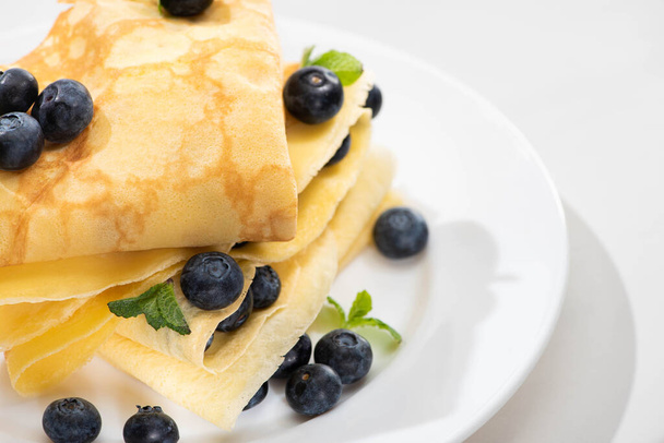 close up view of tasty crepes with mint and blueberries on plate on white background - Photo, Image