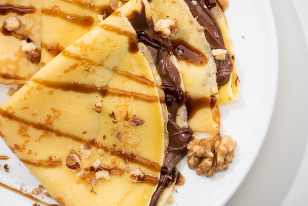 close up view of tasty crepes with chocolate spread and walnuts on plate on white background - Fotó, kép