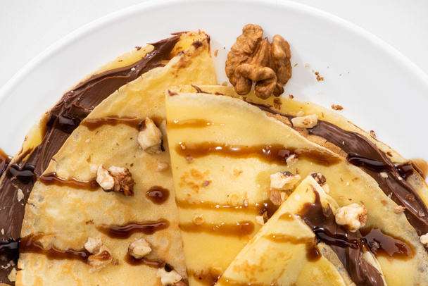 top view of tasty crepes with chocolate spread and walnuts on plate on white background - Fotografie, Obrázek