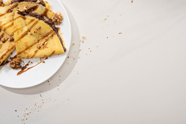 widok z góry smaczne naleśniki z polewą czekoladową i orzechy włoskie na talerzu na szarym tle - Zdjęcie, obraz
