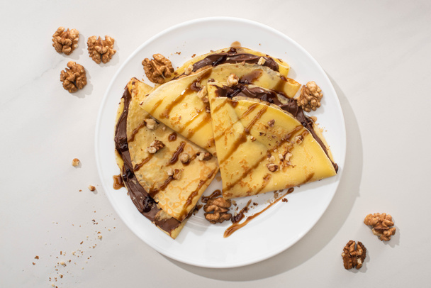 top view of tasty crepes with chocolate spread and walnuts on plate on grey background - Foto, imagen