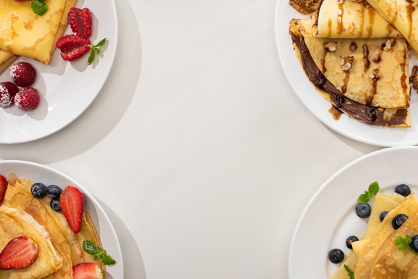 widok z góry smaczne naleśniki z polewą czekoladową, orzechy włoskie i jagody na talerzach na szarym tle - Zdjęcie, obraz
