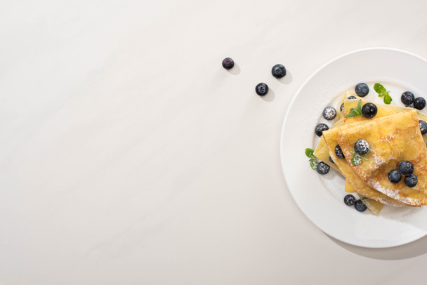 top view of tasty crepes with blueberries and mint on plate on grey background - Fotó, kép
