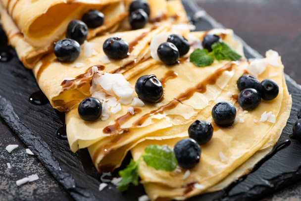 close up view of tasty crepes with blueberries, mint and coconut flakes served on board on textured background - Fotoğraf, Görsel