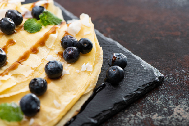 close up view of tasty crepes with blueberries, mint and coconut flakes served on board on textured background - Φωτογραφία, εικόνα