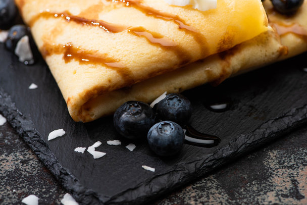 close up view of tasty crepes with blueberries and coconut flakes served on board on textured background - Photo, image