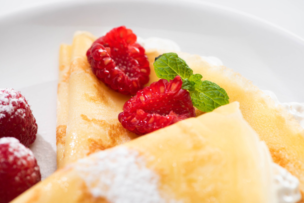 close up view of tasty crepes with raspberries and whipped cream on plate - Photo, Image