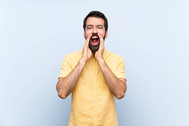 Young man with beard over isolated blue background shouting and announcing something - Foto, imagen