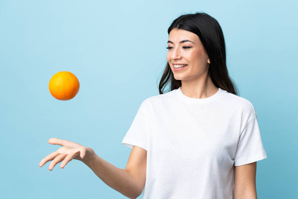 Young brunette girl over isolated blue background holding an orange - Photo, Image