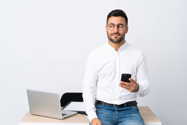 Mladý podnikatel drží mobilní telefon ve stoje a dívá se stranou - Fotografie, Obrázek