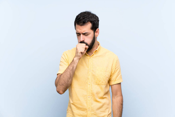 Jovem com barba sobre fundo azul isolado está sofrendo com tosse e se sentindo mal
 - Foto, Imagem