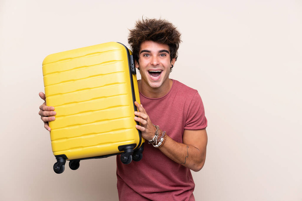Nuori valkoihoinen mies yli eristetty tausta lomalla matkalaukku ja yllättynyt - Valokuva, kuva