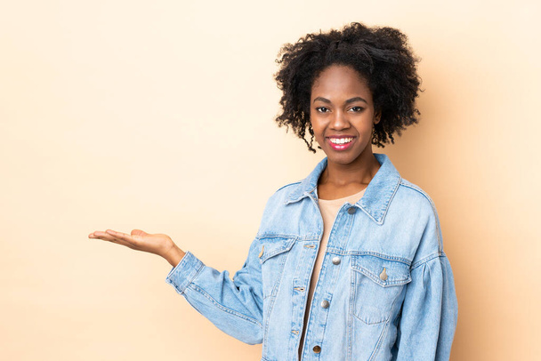 Mladá Afroameričanka izolované na béžové pozadí představuje nápad a zároveň se usmívá směrem - Fotografie, Obrázek