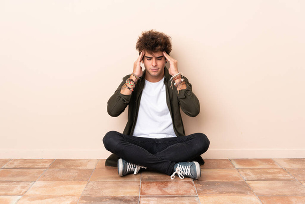 Jonge blanke man zit op de vloer met hoofdpijn - Foto, afbeelding