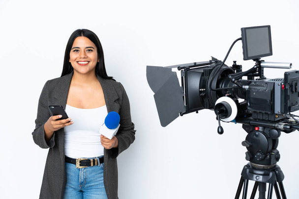 Elinde mikrofon tutan Kolombiyalı gazeteci kadın beyaz arka planda haber sunuyor elinde kahve ve cep telefonu var. - Fotoğraf, Görsel