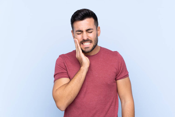 Mladý pohledný muž s vousem přes izolované modré pozadí s bolestí zubů - Fotografie, Obrázek