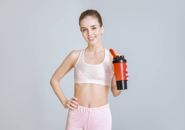 Mujer joven deportiva con batido de proteínas sobre fondo claro
 - Foto, imagen