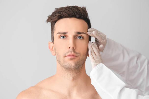 Chirurgien plastique toucher le visage du jeune homme sur fond clair
 - Photo, image