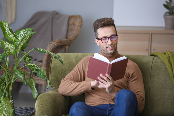 Νεαρός άνδρας με κομψά γυαλιά διαβάζοντας το βιβλίο στο σπίτι - Φωτογραφία, εικόνα
