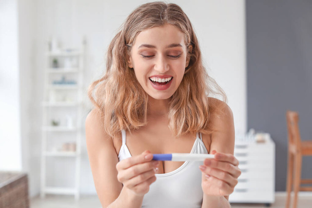 Happy young woman with pregnancy test in bathroom - Photo, Image