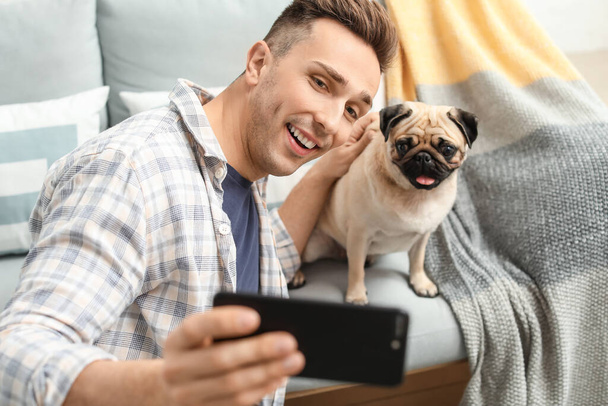 Knappe man neemt selfie met schattige pug hond thuis - Foto, afbeelding
