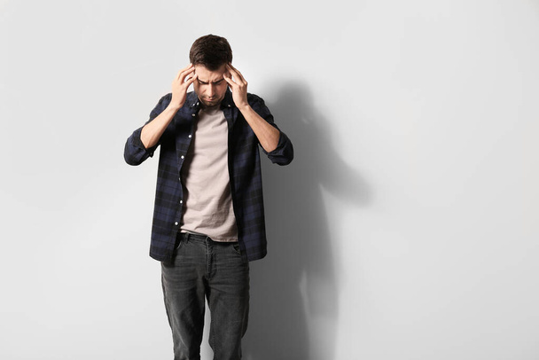 Депрессивный молодой человек возле светлой стены - Фото, изображение