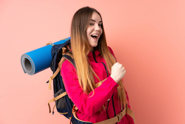 Young mountaineer girl with a big backpack isolated on pink background celebrating a victory - Photo, image
