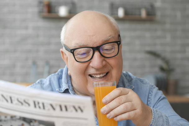 Портрет пожилого человека, пьющего сок во время чтения газет дома
 - Фото, изображение